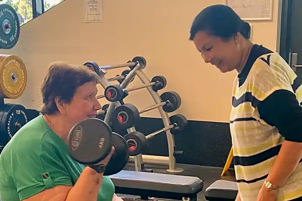 Omega support worker helping elderly lady in the gym
